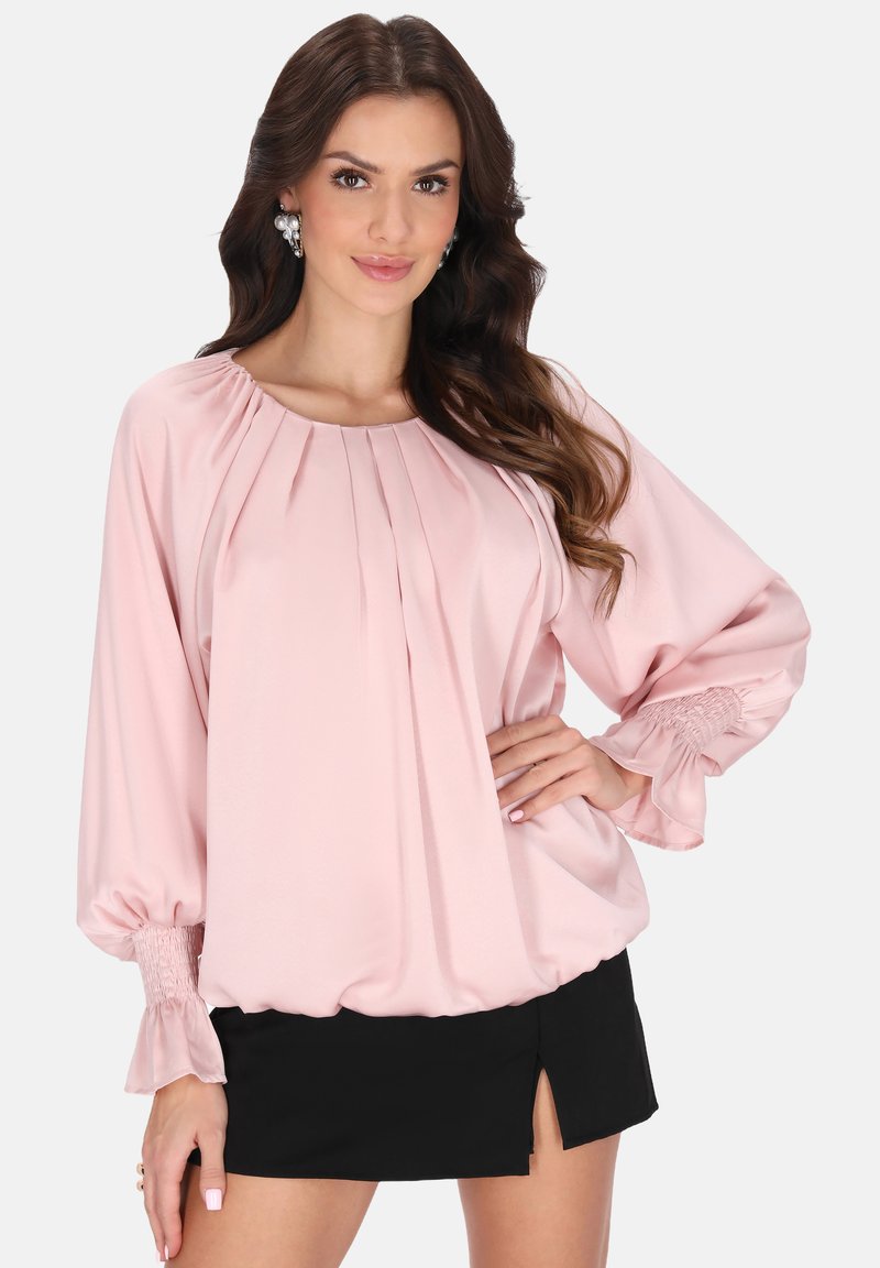 Rosa Satinbluse mit Falten, Ballonärmeln und gesmockten Bündchen, kombiniert mit einem schwarzen Minirock mit seitlichem Schlitz.