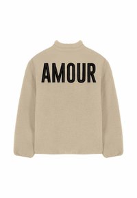Veste polaire beige avec col haut, arborant "AMOUR" en grandes lettres noires dans le dos. Texture douce, coupe décontractée et manches longues.