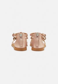 Rózsaszín bőr szandálok, nyitott dizájnnal, hátsó cipzárral és több pánttal. Barna gumitalppal rendelkezik a tapadás érdekében.