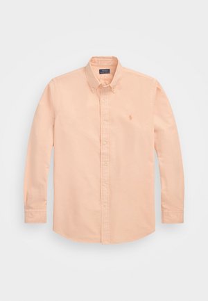 Chemise à manches longues couleur pêche claire avec boutons, col boutonné et petit logo brodé sur la poitrine gauche.