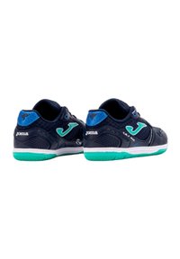 Zapatillas deportivas azul marino con detalles de malla, acentos verdes y una suela blanca. Presenta un logotipo prominente y una superficie texturizada para un mejor agarre.