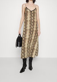 Slangeprint midi kjole i guld og sort med tynde stropper og V-halsudskæring. Parret med sorte hæle støvler og en lille sort håndtaske.