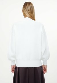 Maglione bianco oversize con scollatura rotonda, spalle scese e polsini a costine. Texture morbida, presenta un design semplice e orlo aderente.