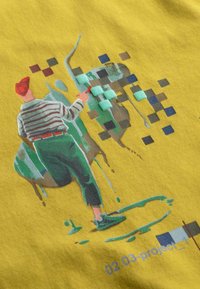 Gele stof heeft een kleurrijk ontwerp van een persoon met een rode hoed en een gestreept shirt die aan het schilderen is, omringd door groene en bruine abstracte vormen.