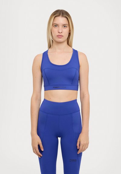 Blue athletic crop top with a scoop neckline and fitted design, paired with matching high-waisted leggings; features logo detail on waist.