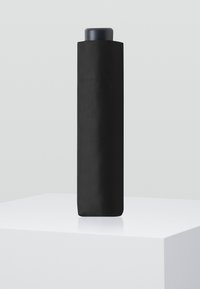 Schwarze zylindrische Wasserflasche mit matter Oberfläche, abgerundetem Deckel und glatter Textur, die auf einem weißen Sockel liegt.