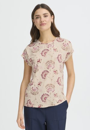 Kurzärmelige Bluse in hellem Beige mit einem Blumenmuster, das lila und grüne Akzente aufweist. Glatte Textur mit rundem Ausschnitt und lockerem Schnitt.