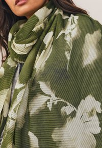 Sciarpa verde con motivo a strisce e texture a coste, decorata con disegni floreali bianchi. Tessuto morbido che avvolge il collo e cade delicatamente.