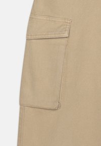 Beige katoenen stof met een zichtbare patchzak en versterkte stiksels, met een gladde, duurzame textuur die geschikt is voor utiliteitskleding.