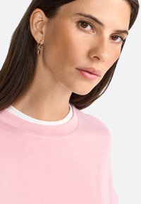 Pink sweatshirt with a round neckline, layered over a white shirt. The fabric appears soft, with smooth texture and minimal stitching details.