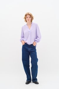 Blusa lavanda con scollatura a V e maniche lunghe a palloncino, abbinata a jeans in denim blu a gamba larga e scarpe slip-on nere.