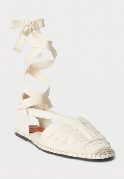 Espadrilles de lona en color blanco roto con lazos de cinta. Presenta un diseño de parte superior tejida, punta redonda y detalles de yute trenzado en la suela.