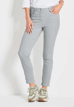 Jeans slim gris clair avec une texture lisse, dotés de poches et d'une fermeture à bouton. Associés à des baskets de couleur claire.