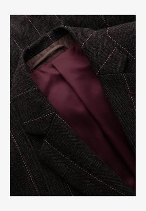 Blazer a righe a spina di pesce scure con cuciture rosa chiaro e fodera in satin borgogna visibile all'interno del rever, che mette in mostra elementi di design su misura.