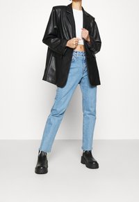 Sort faux læder oversized blazer, hvid crop top, lyseblå lige ben jeans med flossede kanter og kraftige sorte ankelstøvler.