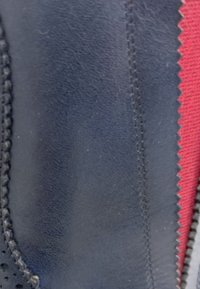 Acercamiento de cuero negro texturizado con costuras detalladas al lado de una tela roja con borde en zigzag.