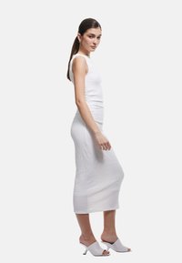 Hvid textureret midi-kjole med en tætsiddende silhuet og tankærmer, parret med lysegrå åbne tå mules. Glat, minimalistisk design.