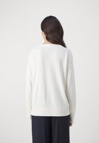 Maglione leggero di colore bianco sporco con una vestibilità rilassata, bordo a costine e scollatura ampia, mostrato da dietro su uno sfondo neutro.
