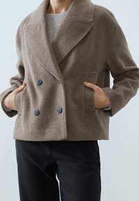 Brun, dobbeltbrystet jakke lavet af blødt stof med en tekstureret overflade, store revers og to sidelommer; knapdetaljer foran.