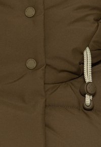 Sección de chaqueta acolchada marrón con dos botones marrones y un cordón con un patrón tejido, creando una apariencia texturizada.