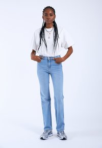 Jeans rectos de color azul claro con una cintura alta, combinados con una camiseta blanca de manga corta y zapatillas deportivas plateadas. Accesorios mínimos visibles.