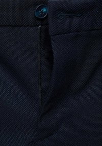Tmavě modrá látka s texturovanou tkaninou, s viditelným zipem a uzavíráním na knoflíky. Materiál se zdá být odolný a strukturovaný.