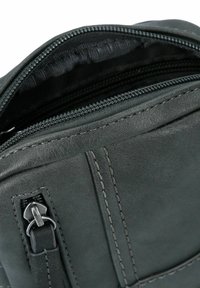 Black leather bag interior with a zippered opening, features smooth texture, contrast stitching, and a small zipper pocket detail.