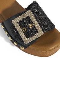 Zwarte geweven slide sandaal met een grote rechthoekige rhinestone gesp, bruine voetbed en gouden studs langs de zijkant.