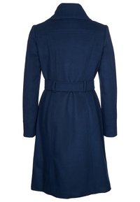 Mörkblå ullrock med skärp i midjan, skräddarsydd silhuett, breda slag och långa ärmar; har vertikala sömdetaljer på baksidan.