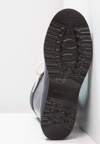 Botte en caoutchouc noire avec des lacets blancs, présentant une semelle extérieure texturée avec un motif rainuré pour une meilleure adhérence. Le profil latéral montre une surface lisse.