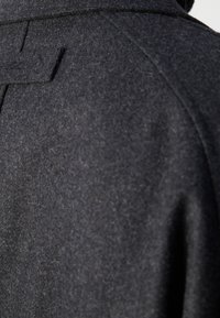 Dos du manteau en laine gris foncé avec un empiècement renforcé et des coutures visibles au niveau des épaules et du col.