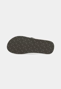Semelle de chaussure en caoutchouc noir avec un motif texturé. La surface présente un design en grille pour une meilleure adhérence et stabilité. Bout arrondi et légère courbure.