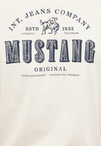 White t-shirt featuring dark blue printed text and a logo with a horse and rider. Text includes "MUSTANG" and "WOVEN WITH HISTORY TAILORED FOR TOMORROW."