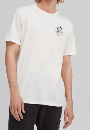 Mann trägt ein weißes kurzärmeliges T-Shirt mit kleinem schwarzem rundem Aufdruck auf der linken Brust, kombiniert mit schwarzer Hose.