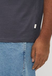 Μπλουζάκι από βαμβάκι σε ναυτικό μπλε χρώμα, με άνετη γραμμή, κοντά μανίκια και μικρή ετικέτα με λογότυπο στη πλευρά, συνδυασμένο με τζιν παντελόνι σε ανοιχτό μπλε.