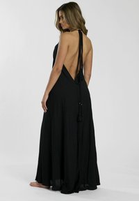 El vestido negro de espalda halter cuenta con una espalda descubierta, una tela fluida y tirantes delgados con borlas. El diseño ofrece una silueta suelta y elegante.