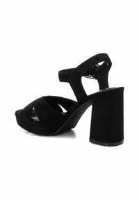 Sandalias de tacón alto de ante negro con un ancho tacón bloque, diseño de punta abierta y detalle de correas entrelazadas. Correa ajustable en el tobillo para un mejor ajuste.