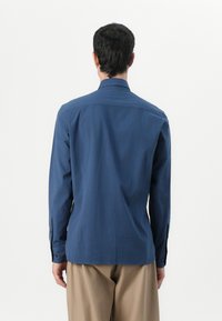 Chemise bleu marine à manches longues avec un col boutonné et des poignets à boutons, fabriquée dans un tissu lisse. Présente un ourlet droit et une coupe décontractée.