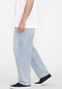 Light blue, straight-leg jeans made from denim, featuring a clean finish with no additional patterns or hardware visible. Worn with black sneakers.
