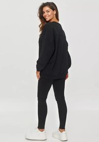Czarny oversizeowy sweatshirt w połączeniu z czarnymi legginsami. Białe sneakersy. Gładka tekstura materiału z luźnym krojem. Tylny widok na strój.