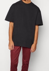 Maglietta nera oversize con maniche corte, scollatura rotonda, realizzata in cotone. Abbinata a pantaloni slim-fit bordeaux, con texture liscia.
