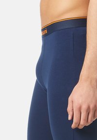 Navy Baumwollleggings mit einem figurnahen Design, ausgestattet mit einem kontrastierenden orangen Taillenbund. Glatte Textur und keine sichtbaren Muster oder Akzente.