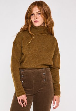 Maglione a collo alto marrone a coste con una vestibilità morbida e colletto arrotolato, abbinato a pantaloni in velluto a coste marroni con dettagli in bottone.