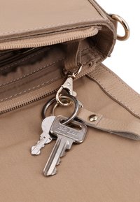 To metalnøgler fastgjort til en nøglering, der er hængt inde i den åbne beige lædertaske med lynlås og syninger.