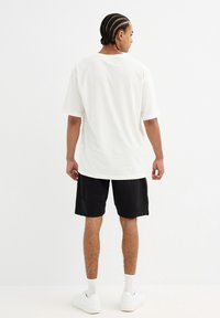 Camiseta de algodón blanca con un corte relajado, combinada con pantalones cortos negros y zapatillas blancas. La tela parece suave, con un diseño simple.