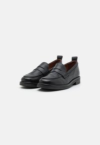 Black leather loafers with a smooth finish, featuring a front strap and a subtle woven detail, accented by a low, textured rubber sole.