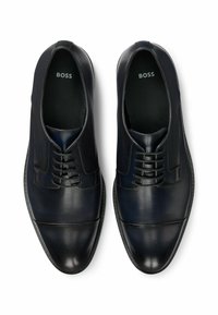 Scarpe eleganti in pelle nera con un design slanciato, punta tonda e dettagli con lacci. Presentano una texture liscia e un marchio discreto all'interno.