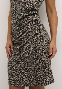 Robe imprimé léopard avec une base beige parsemée de taches noires, confectionnée dans un tissu doux. Le design comporte une texture froncée sur le côté.