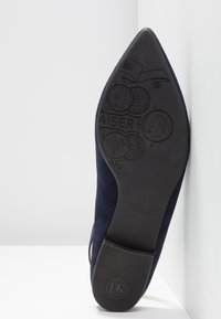 Mørkeblå ruskindssko med spids tå og en tekstureret sort gummisål med præget mønster og mærkedetaljer.