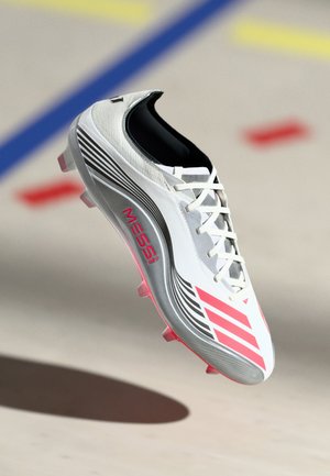 White and gray soccer cleat with pink accents, featuring a sleek design, textured upper, and studded outsole for traction. "MESSI" branding visible.
